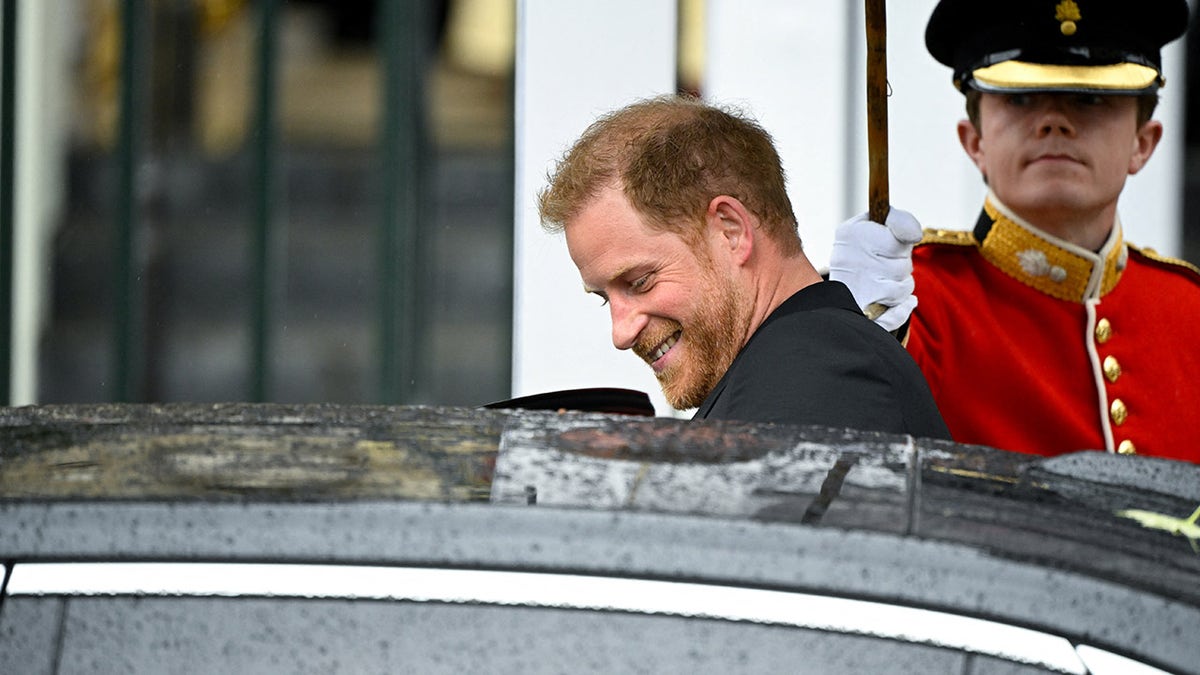 A smiling Prince Harry entering a black car