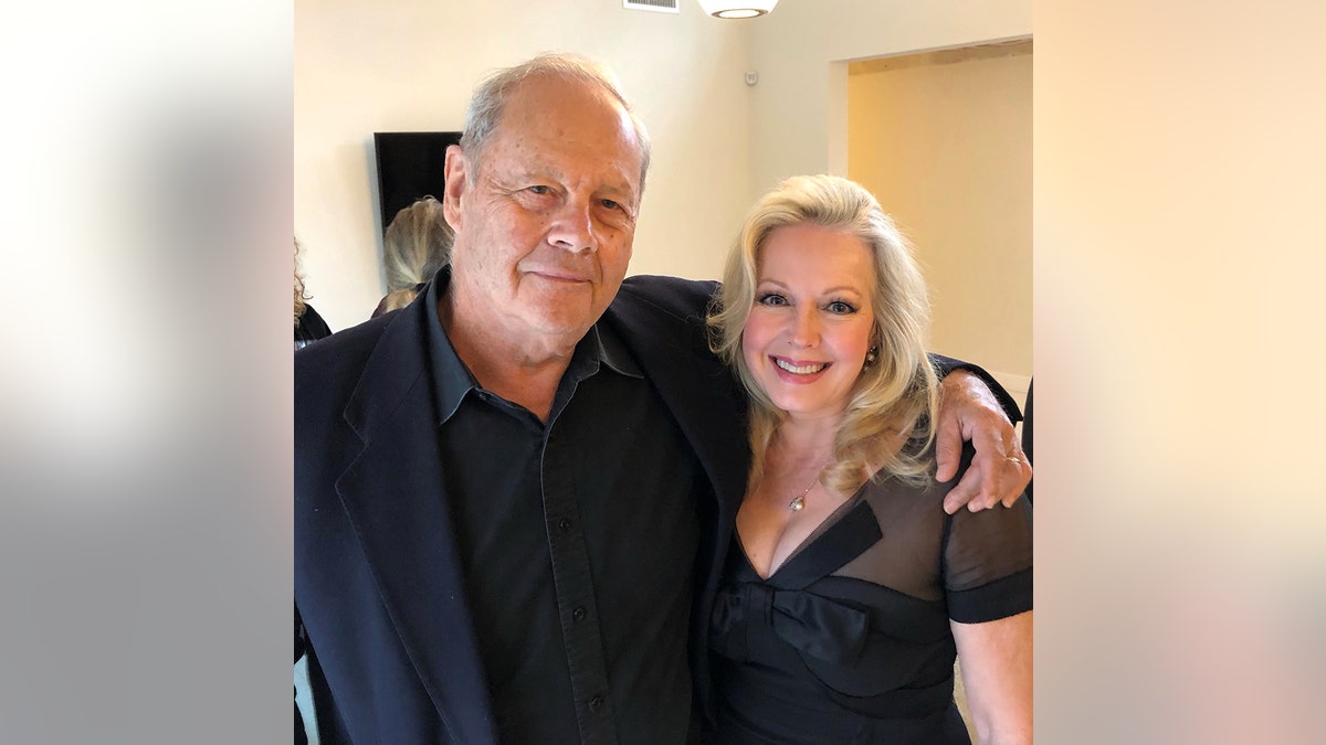 Kym Karath wearing a black dress with her filmmaker who has his arms around her