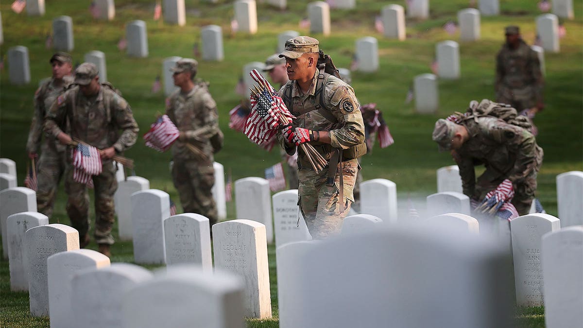 Military members placing flags on tombstones