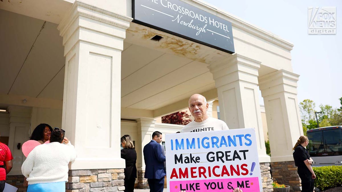Man holds a hand-painted sign in front of the hotel