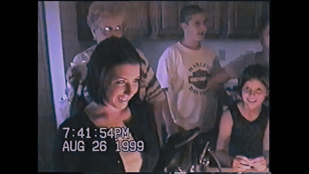 A photo of a home movie showing Judy Malinowski wearing a black sweater