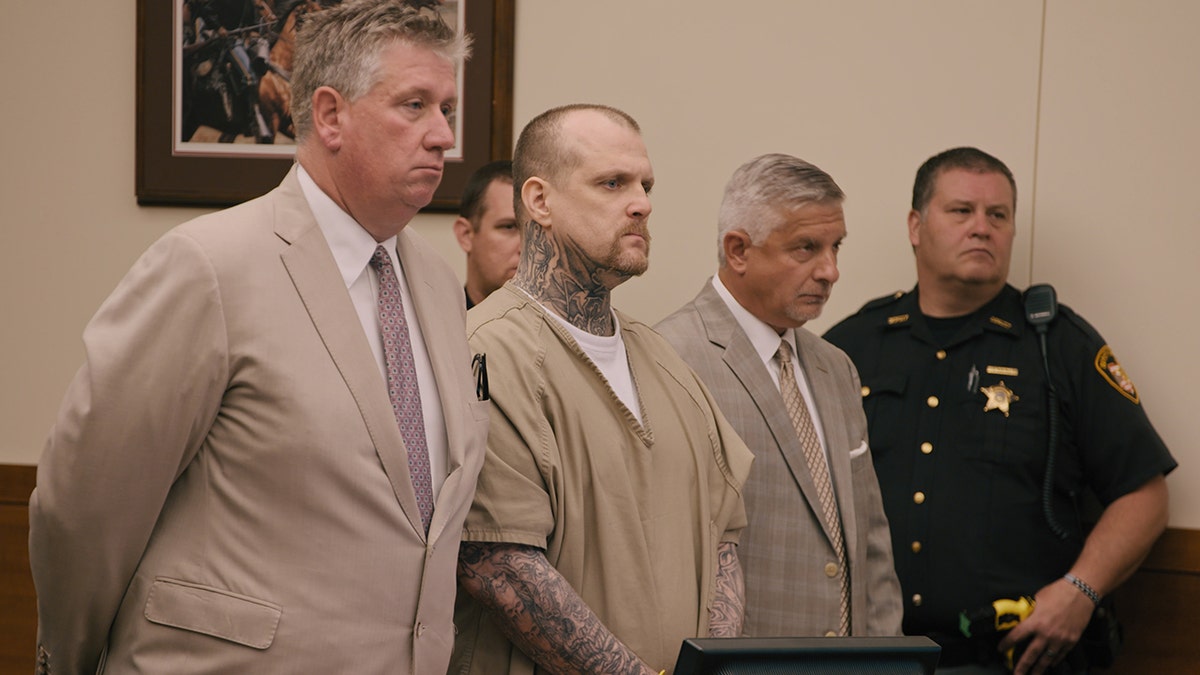 Michael Siager standing up in a beige jumpsuit during trial
