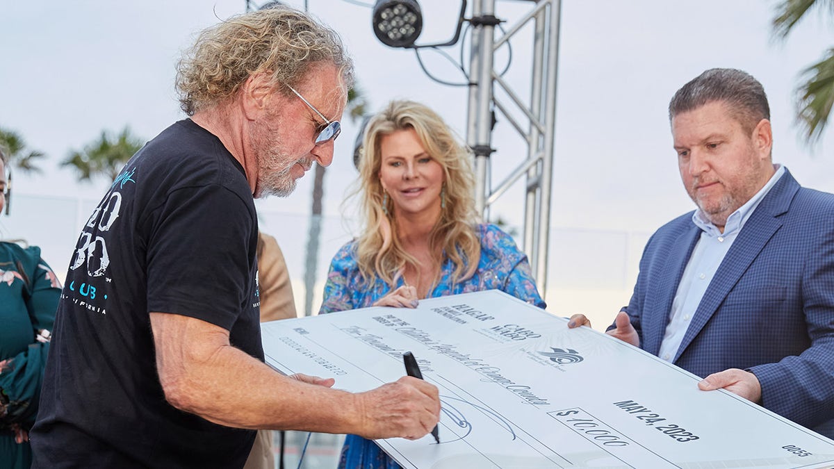 Sammy Hagar signing a check held by his wife Kari