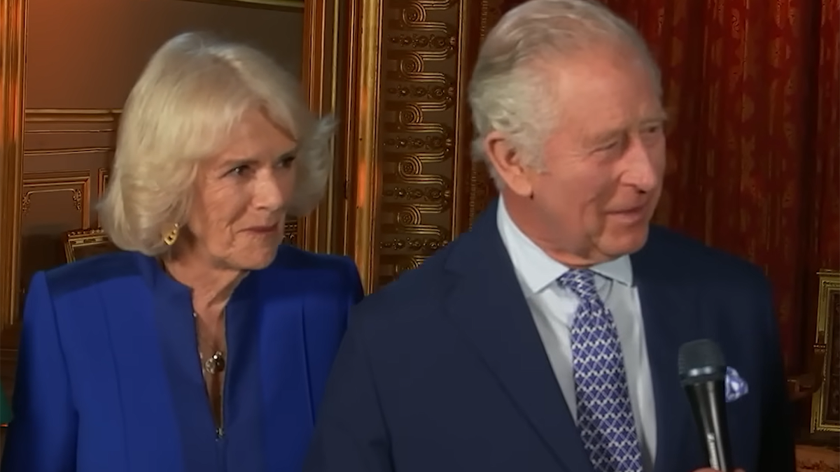 Queen Camilla in a royal blue suit, next to King Charles in a navy suit and blue patterned tie during an episode of "American Idol"