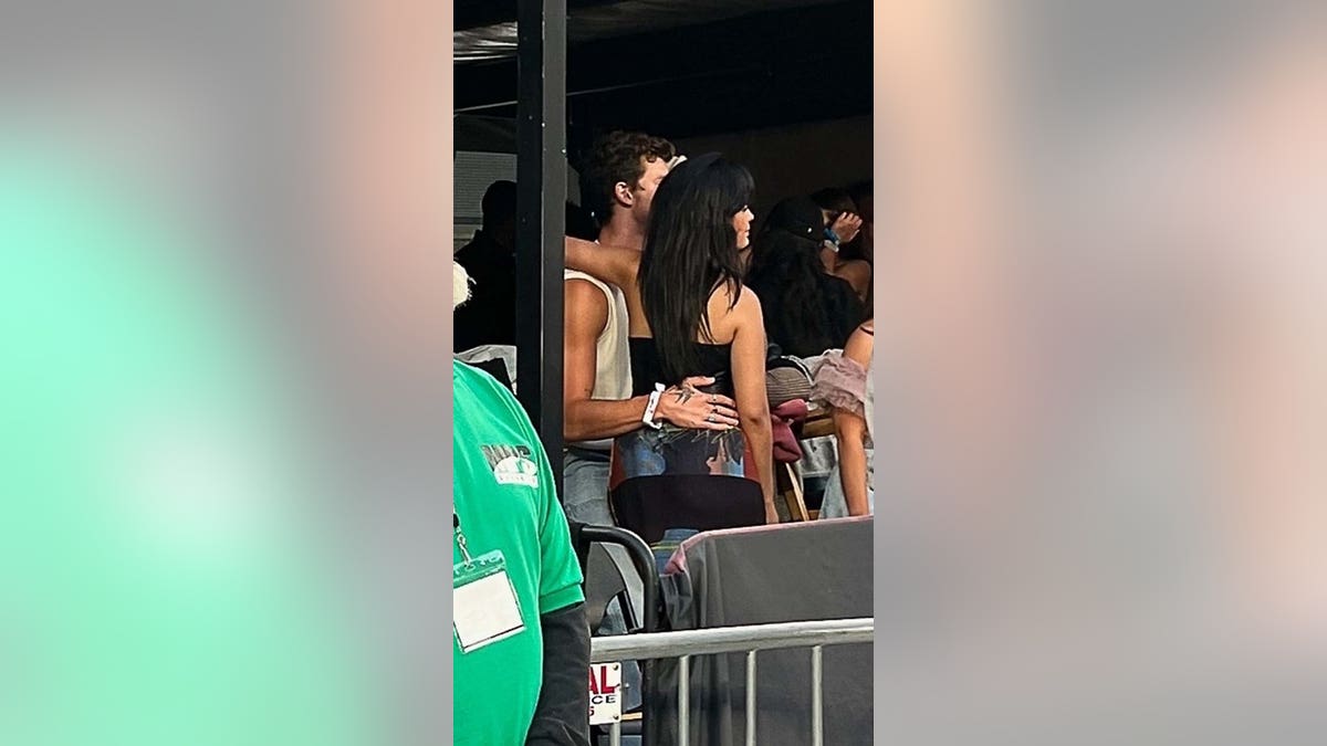 Camila Cabello in black wraps her arm around Shawn Mendes neck with his hand behind her back at the Taylor Swift Era's Tour