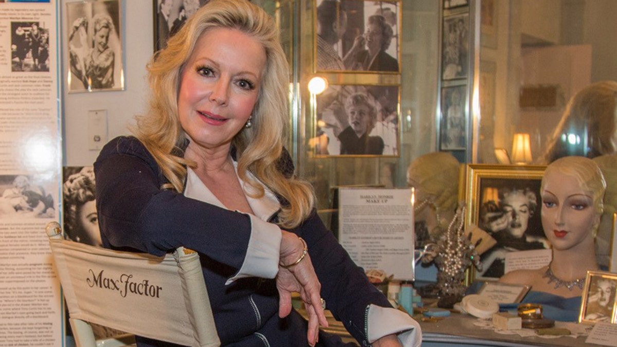 Kym Karath wearing a black and white dress while sitting down in front of a vanity table