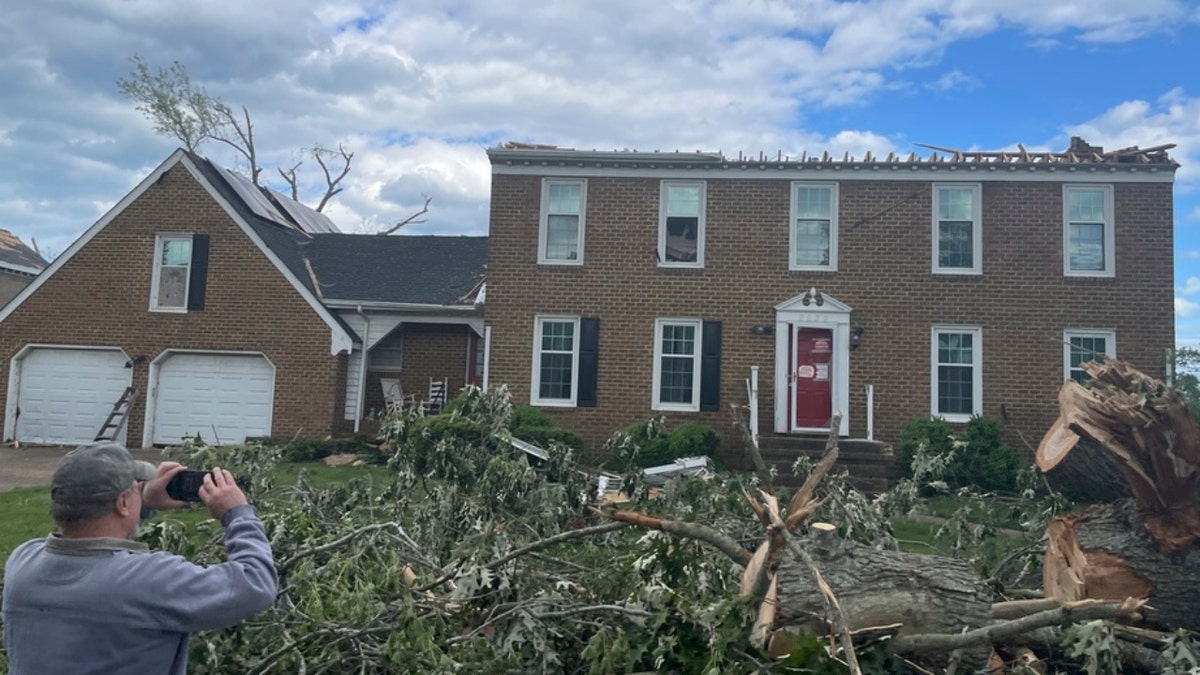 A man photographs a home damaged by a tornado in Virginia Beach