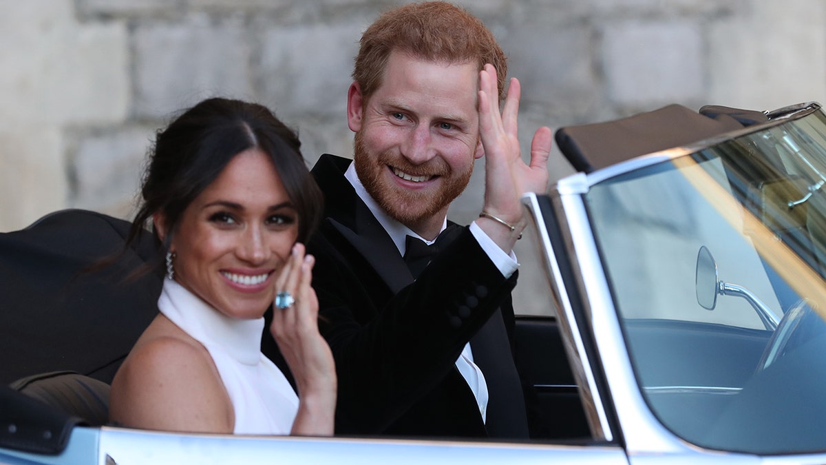 Meghan Markle in a white dress and Prince Harry in a suit waving from their car