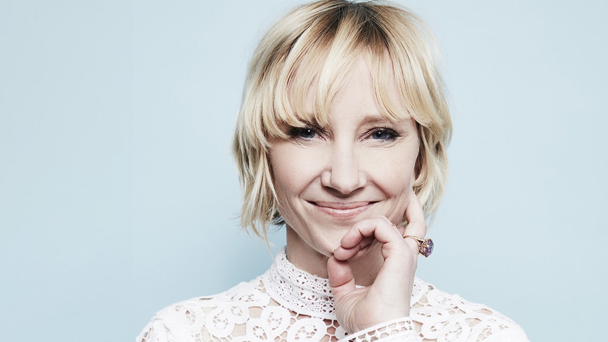 Anne Heche wears white lace top and holds her hand up to her head.