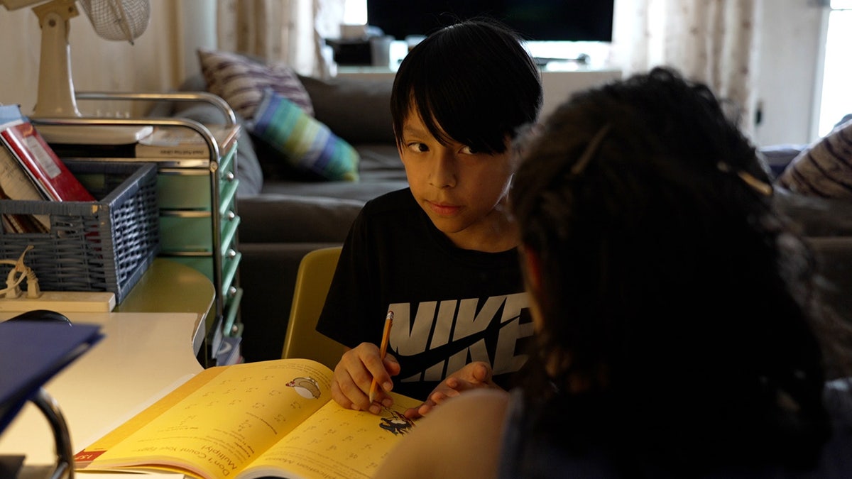 Homeschool mother and her son sit with math workbook open between them