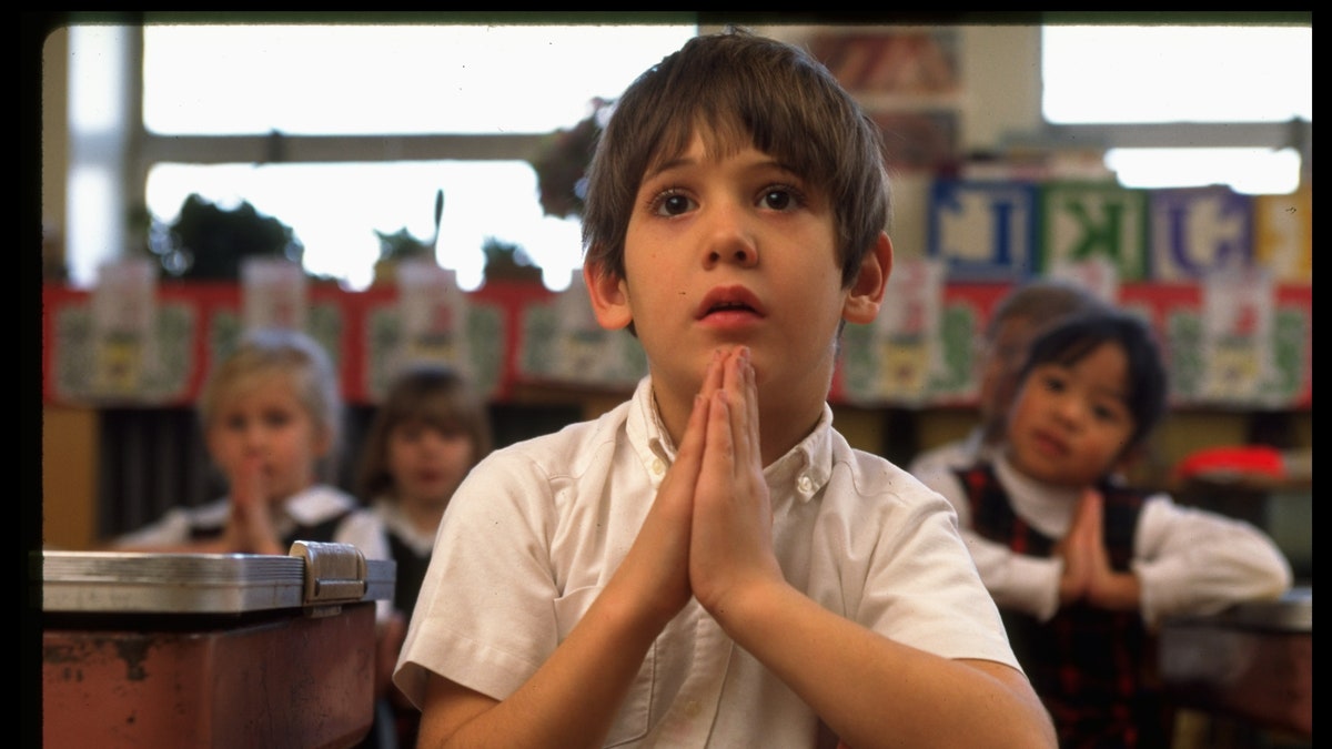 Boy clasping hands, saying prayers in first grade class at St. Gertrude's elementary school.