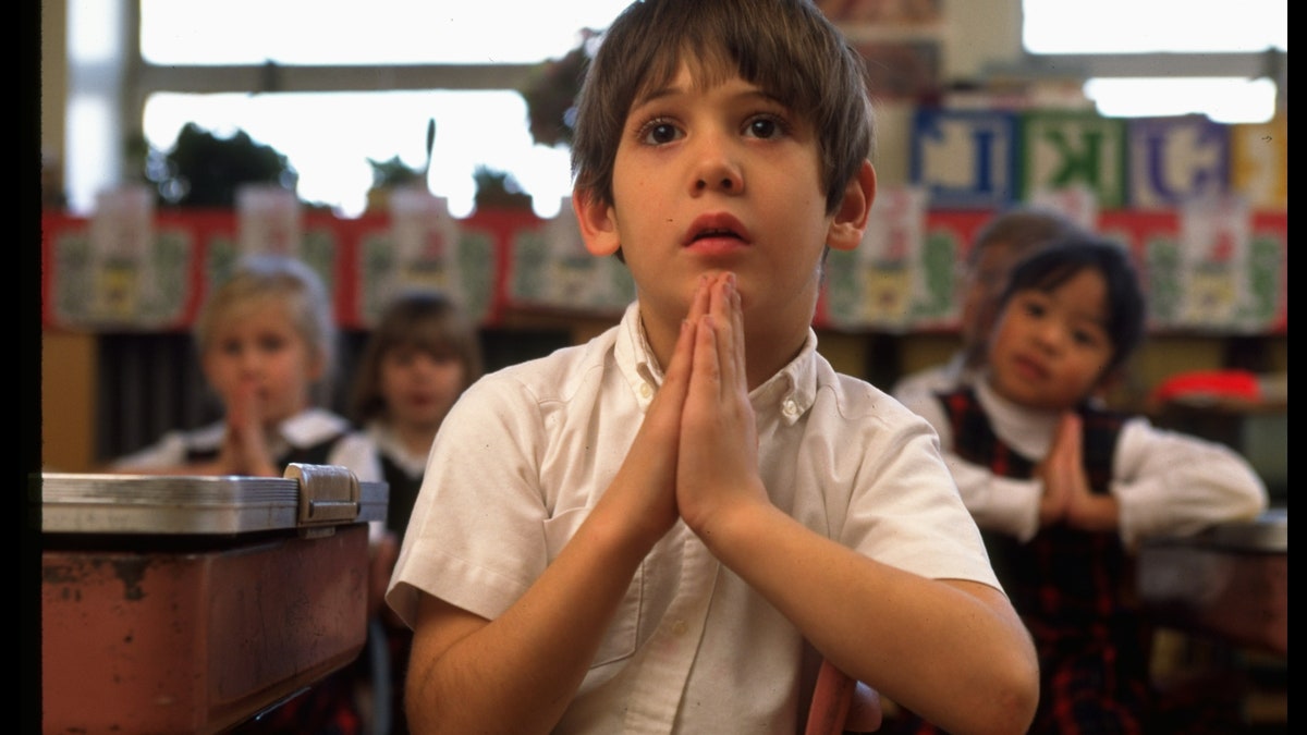 Boy clasping hands, saying prayers in first grade class at St. Gertrude's elementary school.