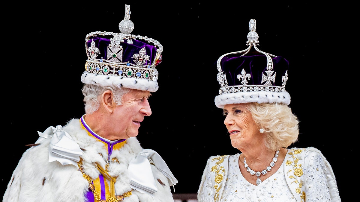 King Charles in his royal regalia looking at Camilla in a white gown wearing a crown