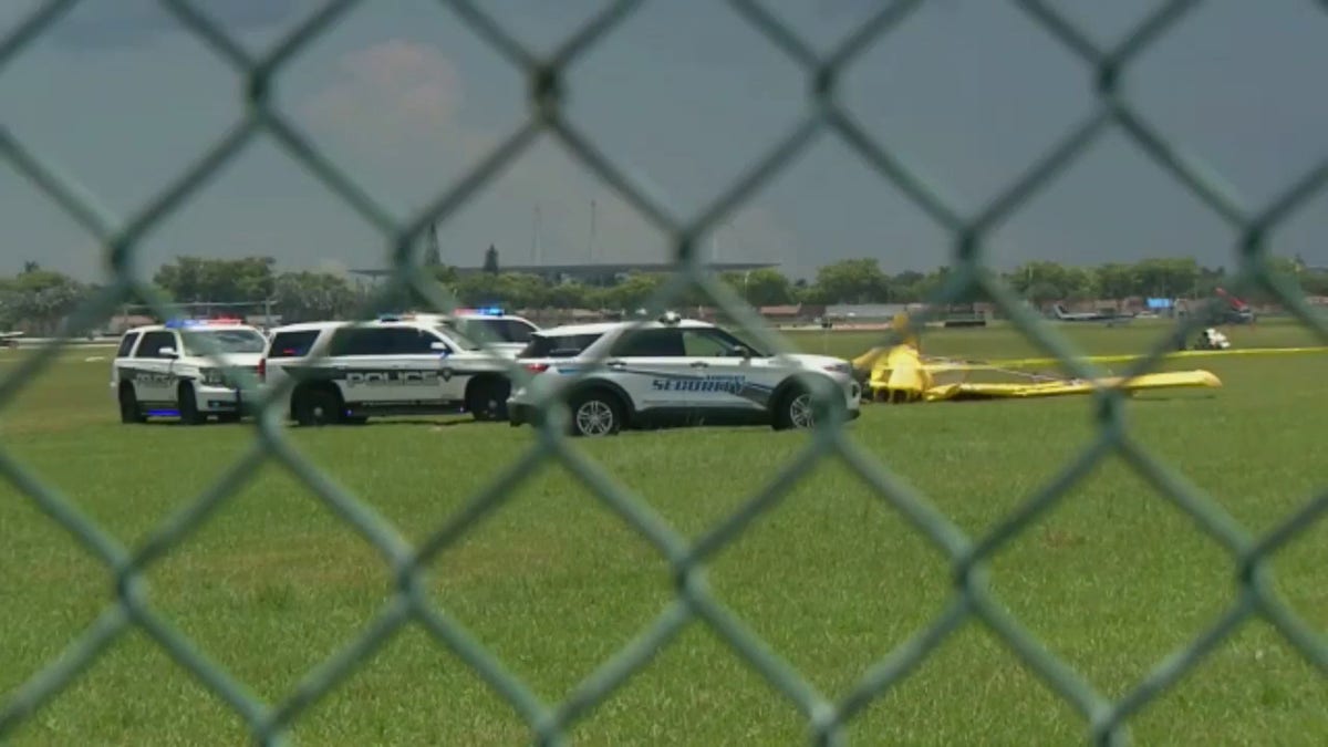 Airport security vehicles are seen next to the crashed plane through a chain-linked fence