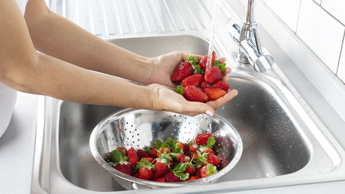 A mulher está lavando morango na pia da cozinha.