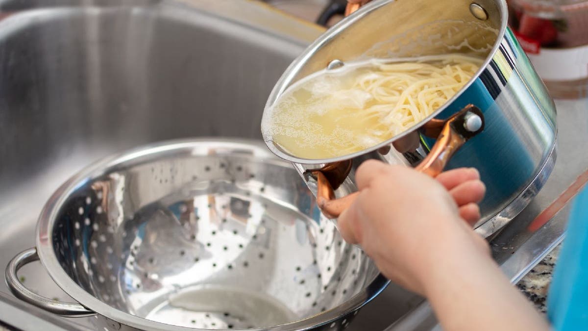Woman separates water from spaghetti with an empty metal colander.