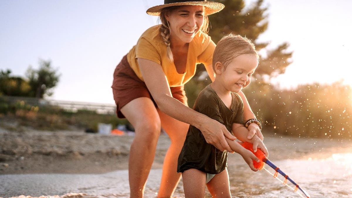 Mother and cute little toddler playing with fishing toy on the sea.