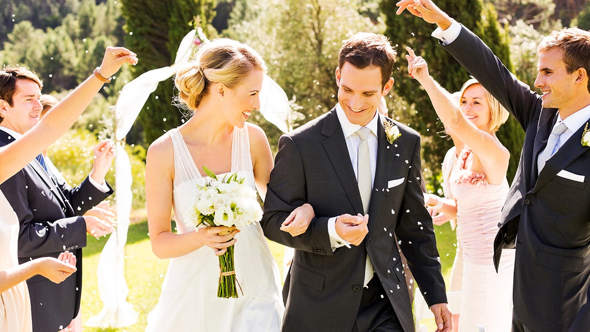 Happy couple walking while guests throwing confetti on them during wedding ceremony.