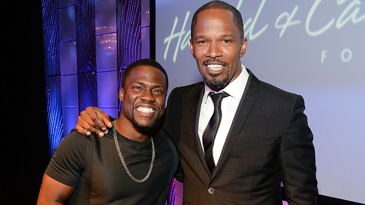 Jamie Foxx wears a black tuxedo with Kevin Hart wearing a black shirt at celebrity event.