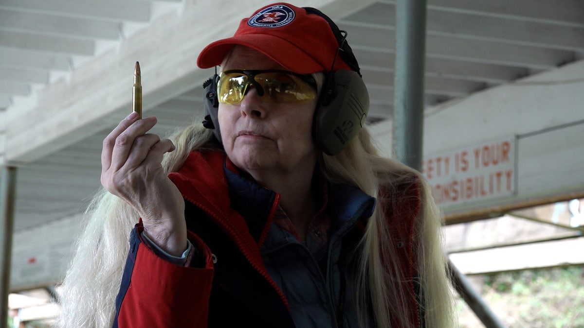 A female firearms instructor holds up a bullet for a bolt-action rifle