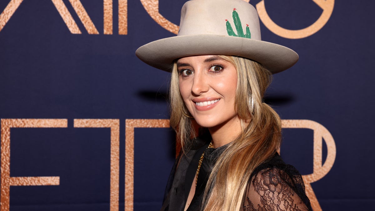 Lainey Wilson smiles for a photo wearing a large cowboy hat.