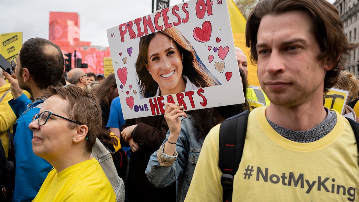 A protesters holding a sign calling Meghan the "princess of hearts"