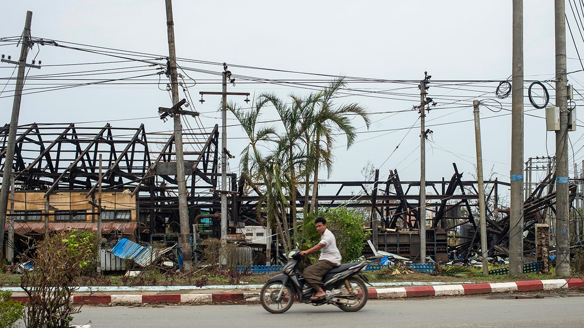 man rides motorbike past damaged buildings