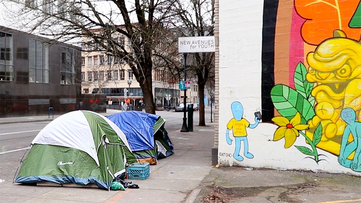Tents cover a sidewalk in Portland next to a brightly-colored mural