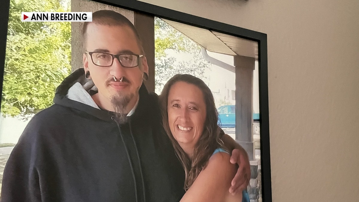 A young man in glasses wraps his arm around an older woman who is smiling and is his mother