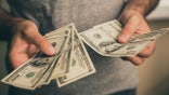 A man in a gray T-shirt holds dollars in his hands. Bank. Casino. Salary. Rates.