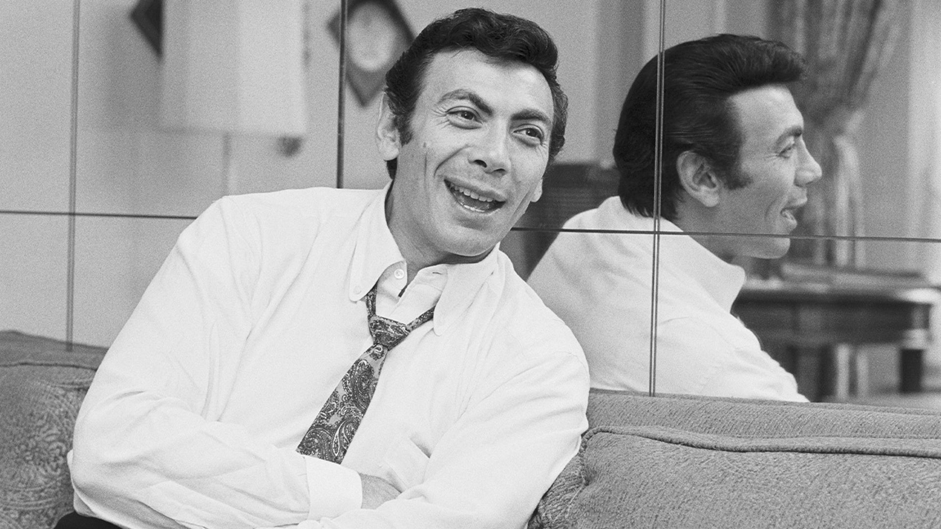 Ed Ames sitting next to a mirror and smiling