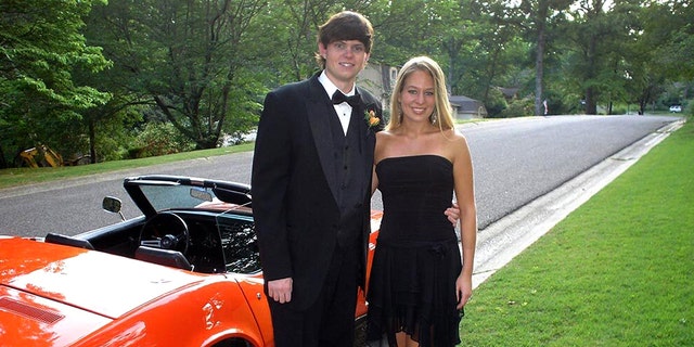 Henry in a tuxedo, Natalee in a short black dress, the pair stand in front of a convertible red muscle car