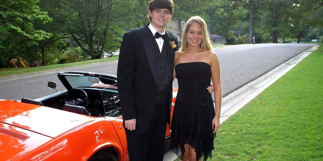 Henry in a tuxedo, Natalee in a short black dress, the pair stand in front of a convertible red muscle car