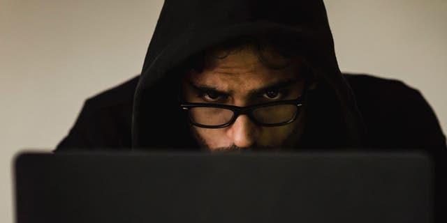 رجل يرتدي قلنسوة سوداء مع نظارات تحوم فوق كمبيوتر محمول أسود