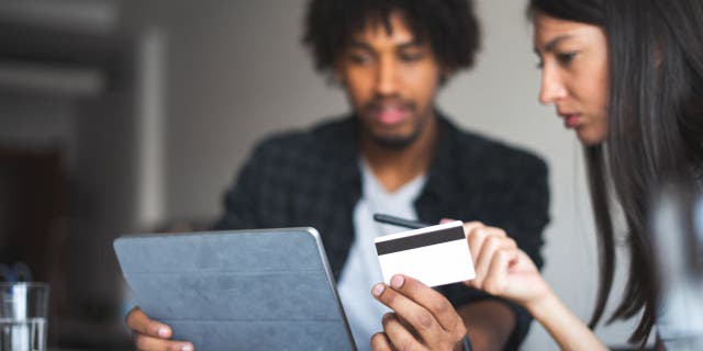 Couple holds credit cards while working on a computer