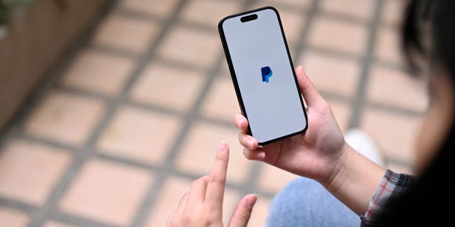 Woman holding her phone while loading the PayPal app.