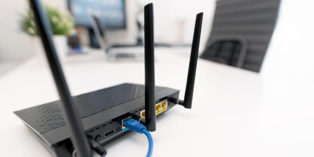 Black wifi router on white desk near computer monitors 