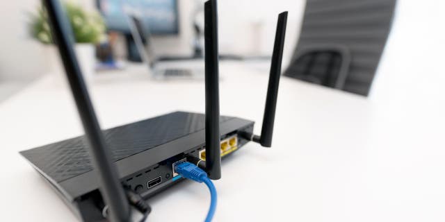 Black wifi router on white desk near computer monitors 