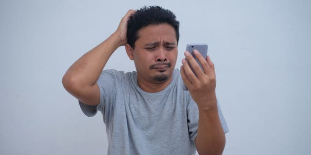 Upset man rubs his head while on his phone