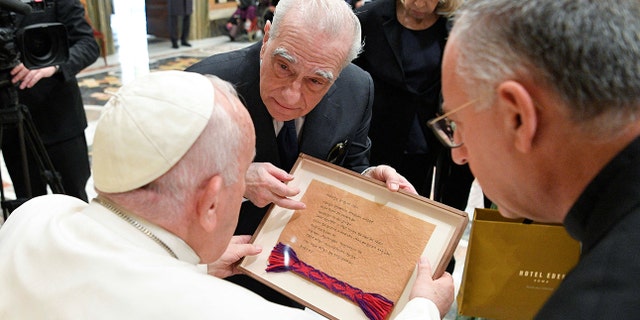 Pope Francis looks down at a frame that Martin Scorsese has presented him with