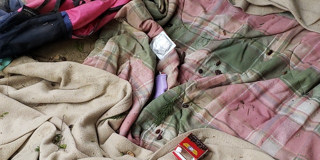 Unused condom packet next to purple lighter on pink and green flannel blanket