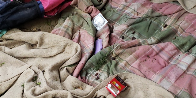 Unused condom packet next to purple lighter on pink and green flannel blanket