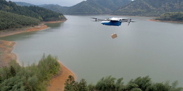 Photo of a drone carrying a box over a lake.