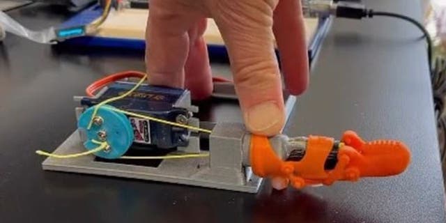 Orange 3D-printed prosthetic pinky on a contraption with man's hand on top