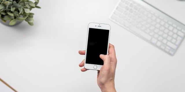 A person holing their phone over a white desk.