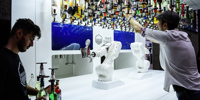 Two men look on as a robot prepares cocktails.