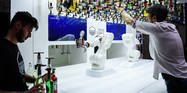 Two men look on as a robot prepares cocktails.