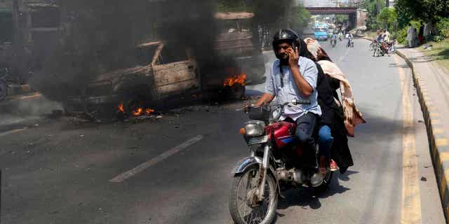 A motorcyclist drives past a burning vehicle