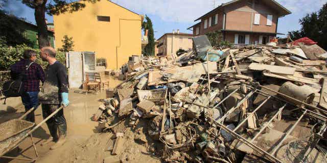 Volunteers clear mud as household goods are piled on the side of a street in Faenza, Italy,