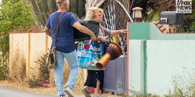 Joran van der Sloots mom, Anita carries a drum in her right hand, a water bottle under her arm, her male friend carries a big bluetooth speaker